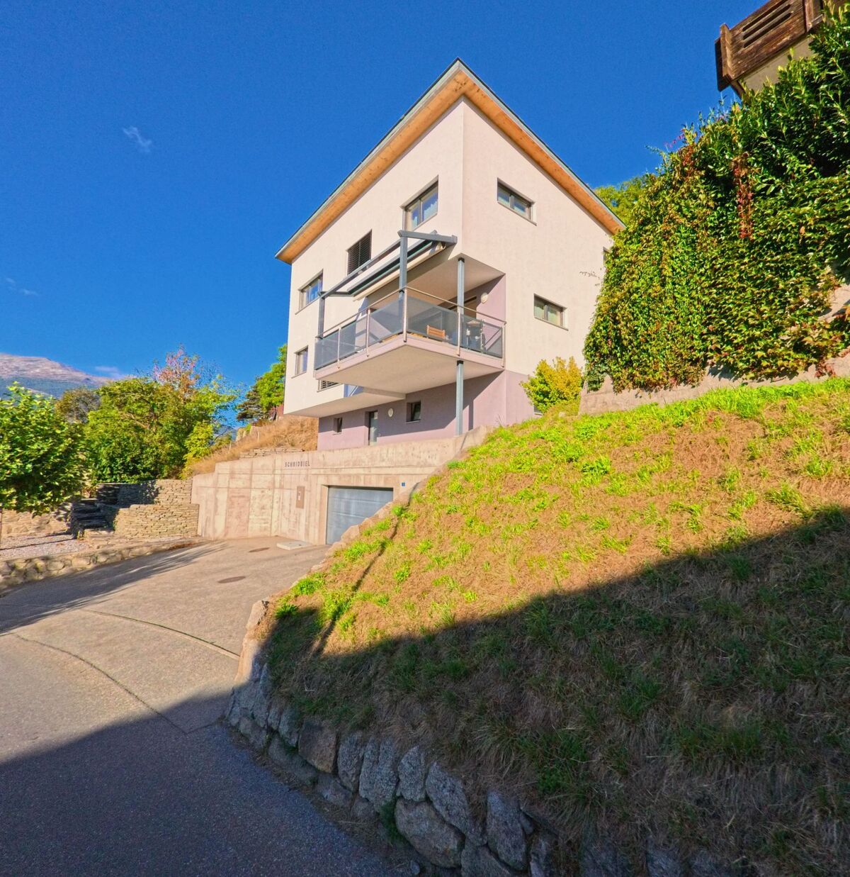 Ein modernes Wohnhaus mit Balkon und Garage erhebt sich am steilen Hang in Ausserberg (3938, Kanton Wallis).