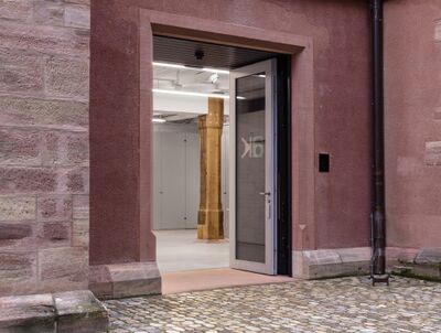 Der Eingang zum Ausstellungsraum Klingental in Basel (4058, Kanton Basel-Stadt) zeigt eine geöffnete Tür in einem sandfarbenen Steinbau.