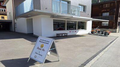In Tujetsch (7188, Kanton Graubuenden) befindet sich das Baan Na Restaurant & Take Away in einem modernen Gebaeude mit grossem Schaufenster und Hinweisschild vor dem Eingang.