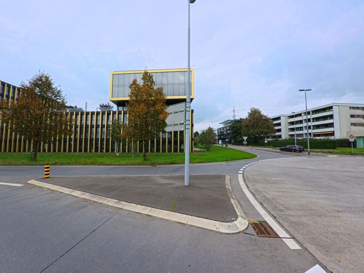 In Baar (6319, Kanton Zug) treffen moderne Buero- und Wohngebaeude an einer grosszuegigen Kreuzung aufeinander, flankiert von herbstlichen Baeumen.