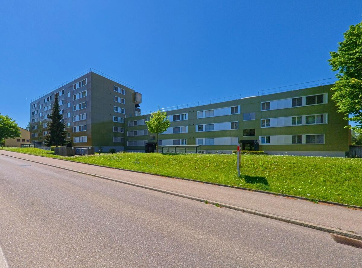 In Bachenbülach (8184, Kanton Zürich) stehen moderne Wohnblocks mit flachen Fassaden und grosszügigem Grünstreifen entlang der Strasse.