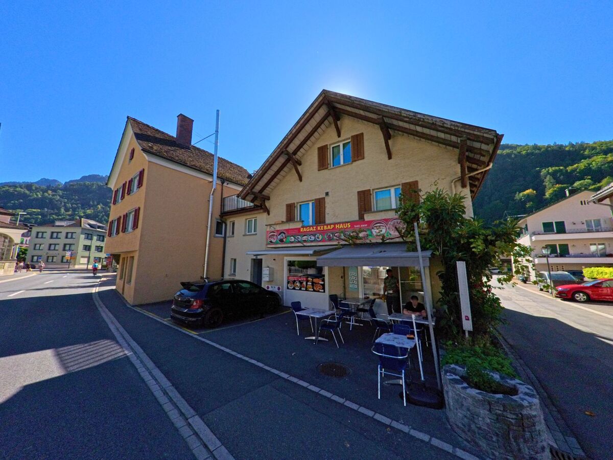 Ein kleines Restaurant mit Aussenterrasse und hölzernen Fensterläden steht in Bad Ragaz (7310, Kanton St. Gallen) an einer Strassenecke mit Blick auf bewaldete Hügel.
