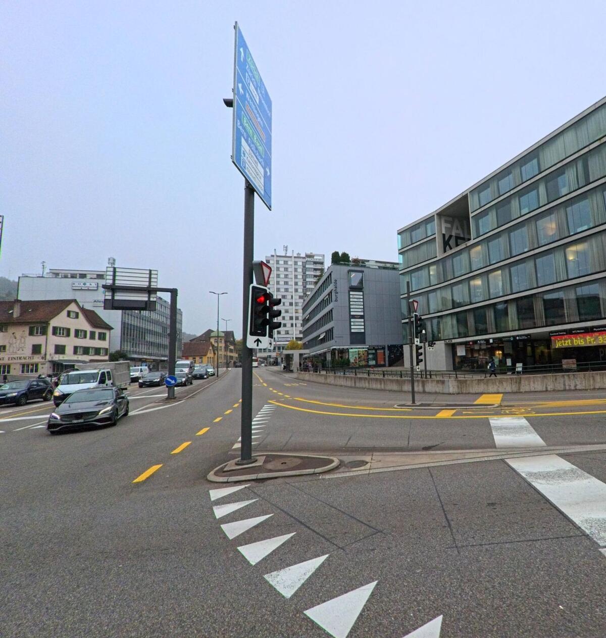 Im Stadtzentrum von Baden (5400, Kanton Aargau) fuehrt eine Hauptstrasse mit Ampeln und modernen Buerogebaeuden zwischen dichter Bebauung hindurch.