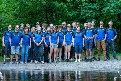 Mitglieder des Badminton Clubs Gränichen aus Gränichen (5722, Kanton Aargau) stehen gemeinsam in blauer Vereinskleidung vor einer grünen Waldkulisse.