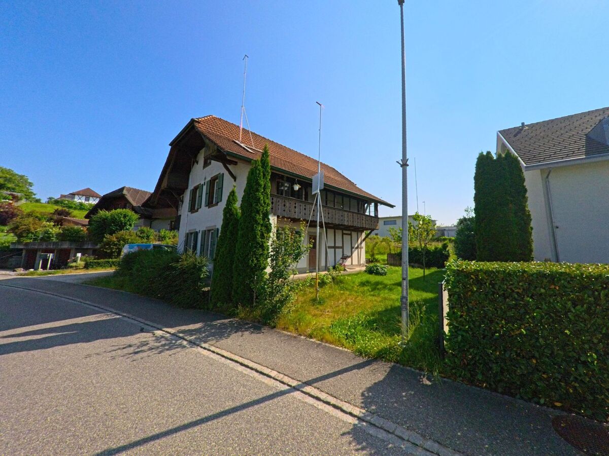 Ein traditionelles Wohnhaus mit grünem Fensterläden und Holzbalkon steht in Bäriswil (3323, Kanton Bern) an einer ruhigen Strasse mit gepflegtem Vorgarten.