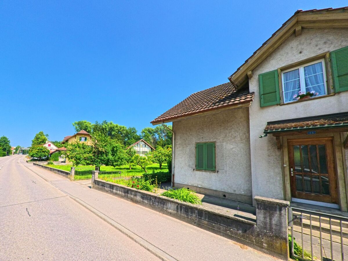 Entlang einer leicht ansteigenden Strasse in Bätterkinden (3315, Kanton Bern) reihen sich Einfamilienhäuser mit gepflegten Vorgärten und Fensterläden in sattem Grün.