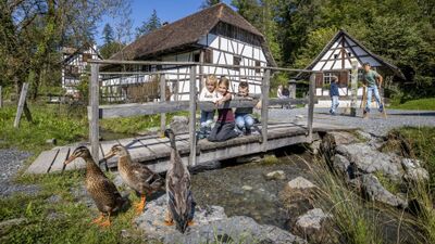 Im Ballenberg Freilichtmuseum der Schweiz in Hofstetten bei Brienz (3858, Kanton Bern) beobachten Kinder auf einer Holzbruecke Enten vor traditionellen Fachwerkhaeusern.