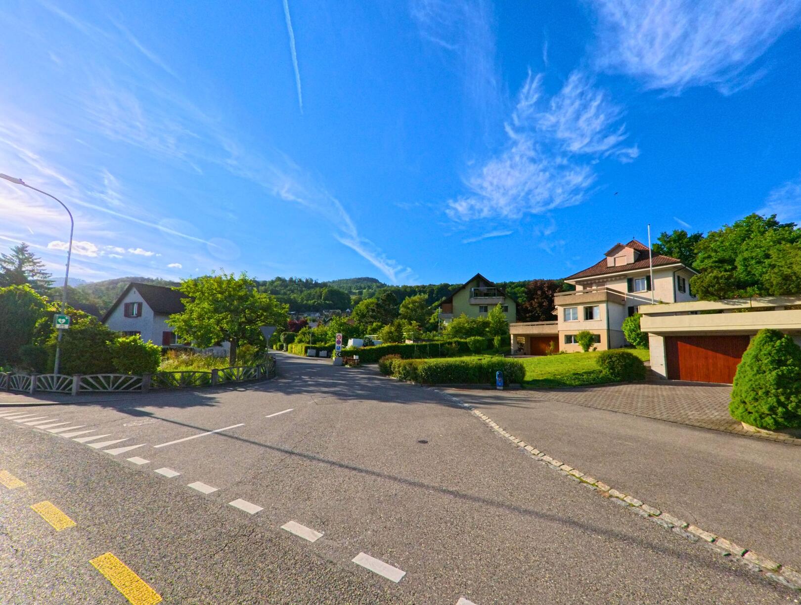 Am Ortsrand von Balsthal im Kanton Solothurn, PLZ 4710, verläuft eine Landstrasse an einer Felswand und einem einfachen Gebäude vorbei mit Blick auf eine grüne Wiese und bewaldete Hügel.