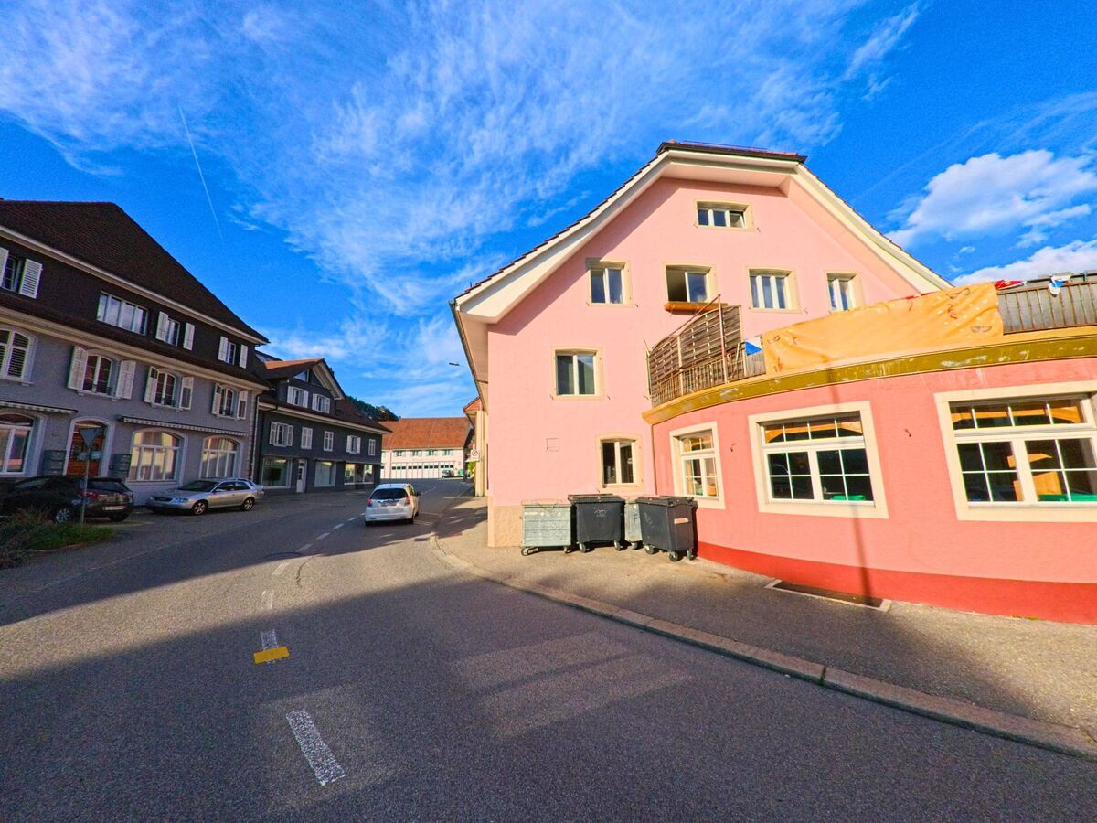 In der Gemeinde Balsthal im Kanton Solothurn, PLZ 4710, verläuft eine schmale Strasse zwischen mehrstöckigen Wohnhäusern, darunter ein auffällig rosafarbenes Gebäude mit Balkon.