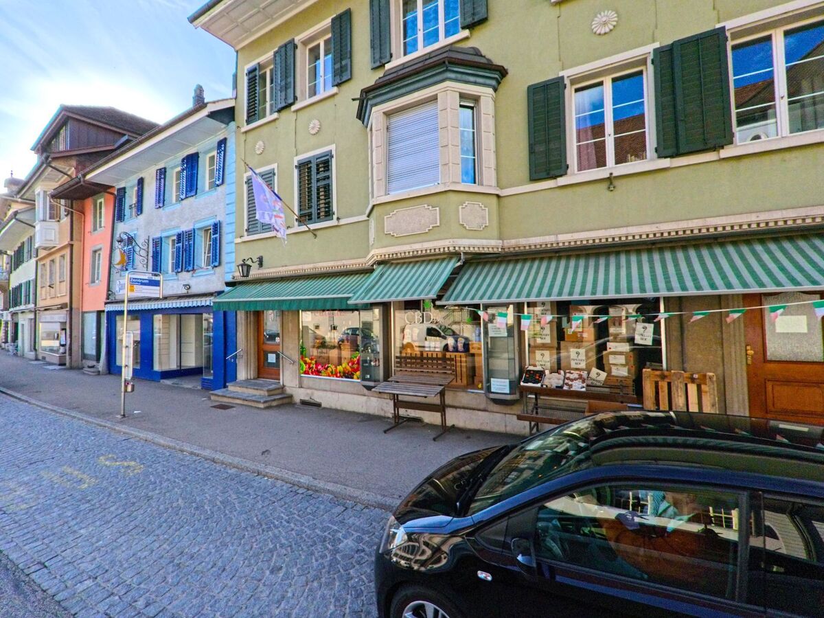 In der Altstadt von Balsthal im Kanton Solothurn, PLZ 4710, reihen sich farbige Häuser mit Läden und Markisen entlang einer gepflasterten Strasse.