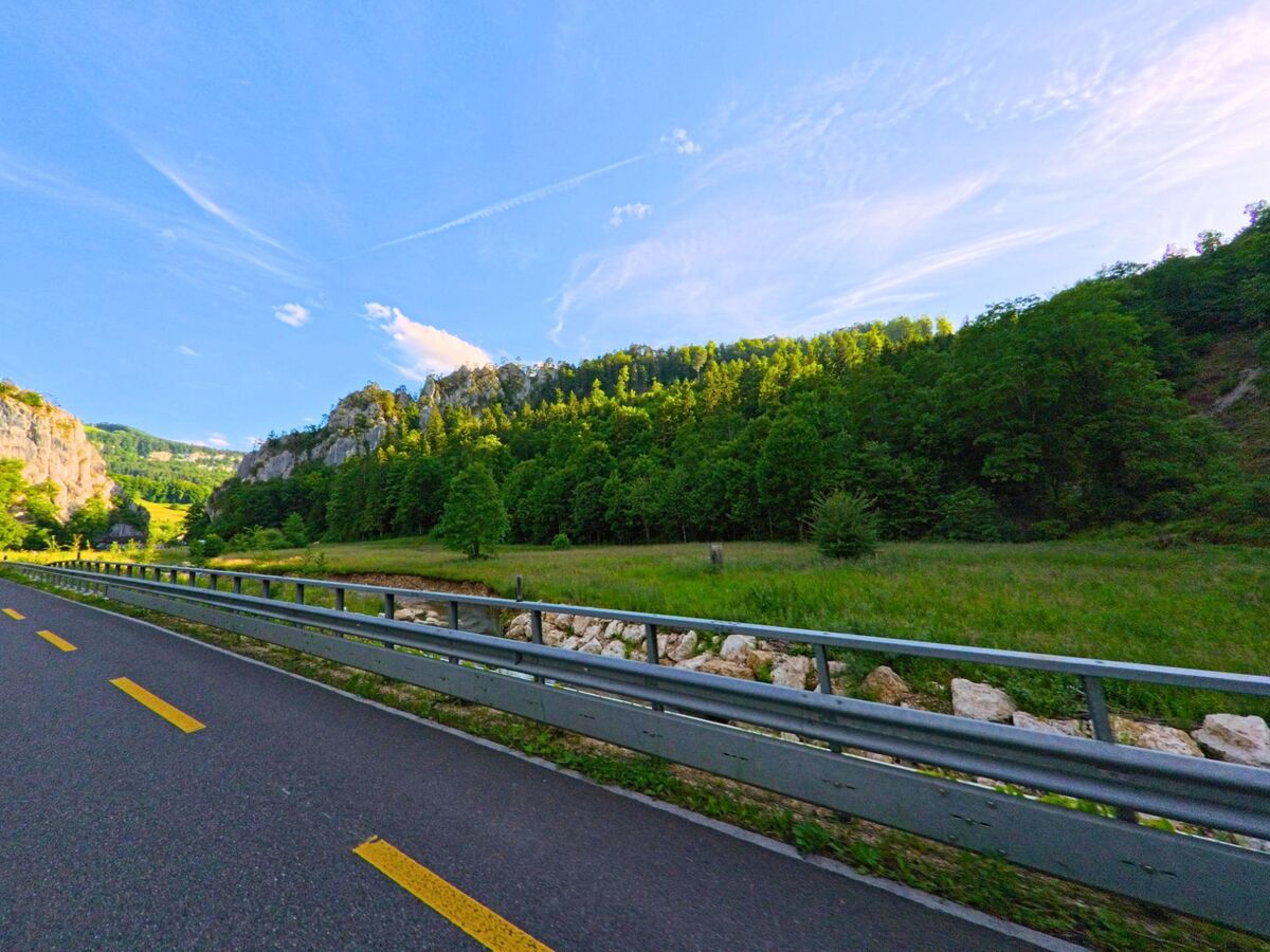 Am Ortsausgang von Balsthal im Kanton Solothurn, PLZ 4710, verläuft eine gut ausgebaute Strasse mit Leitplanke entlang bewaldeter Felsformationen und grüner Wiesenlandschaft.