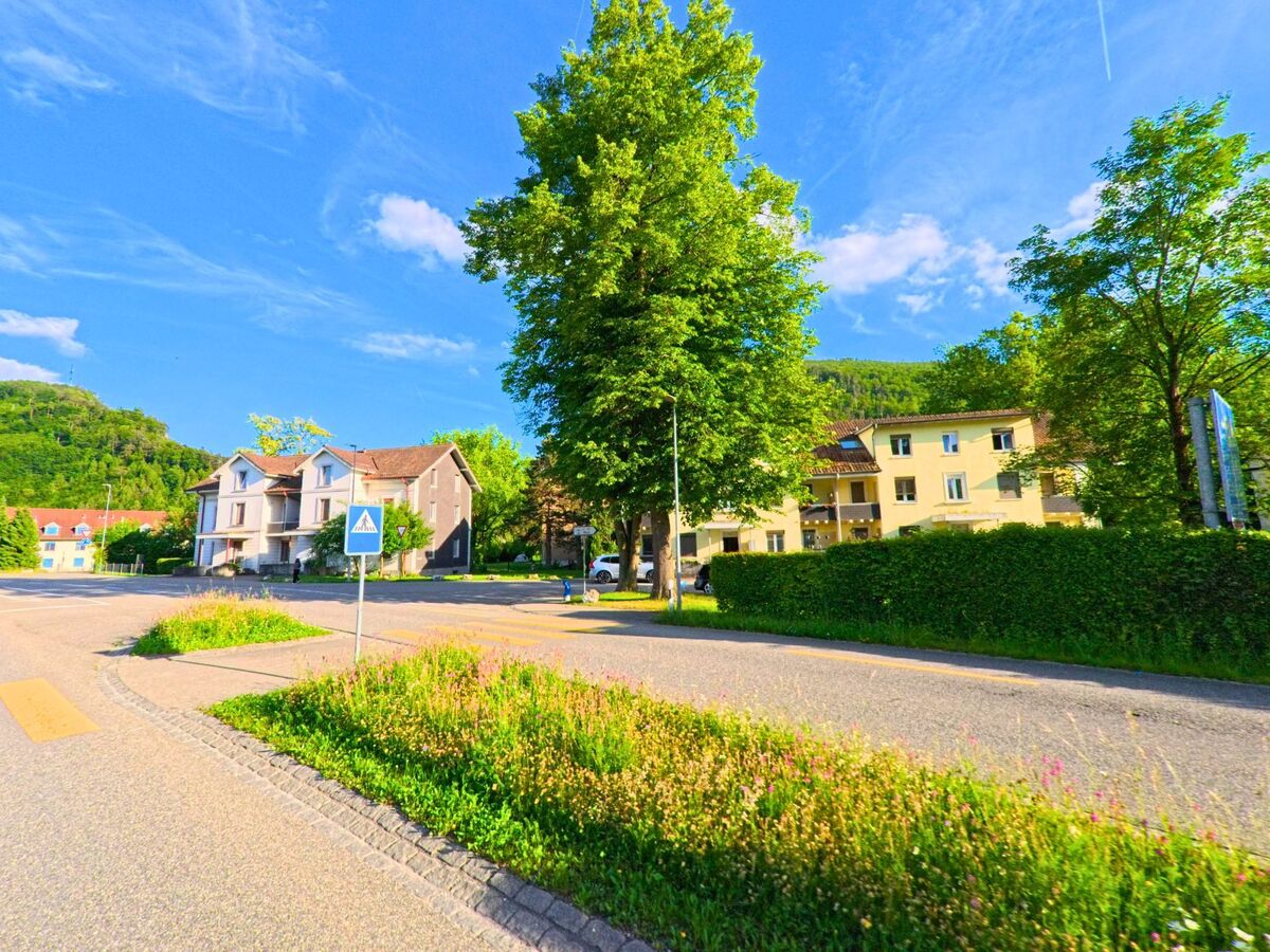 Im Zentrum von Balsthal im Kanton Solothurn, PLZ 4710, säumen ältere Wohnhäuser und ein Fussgängerstreifen eine begrünte Verkehrsinsel an einer breiten Strasse.