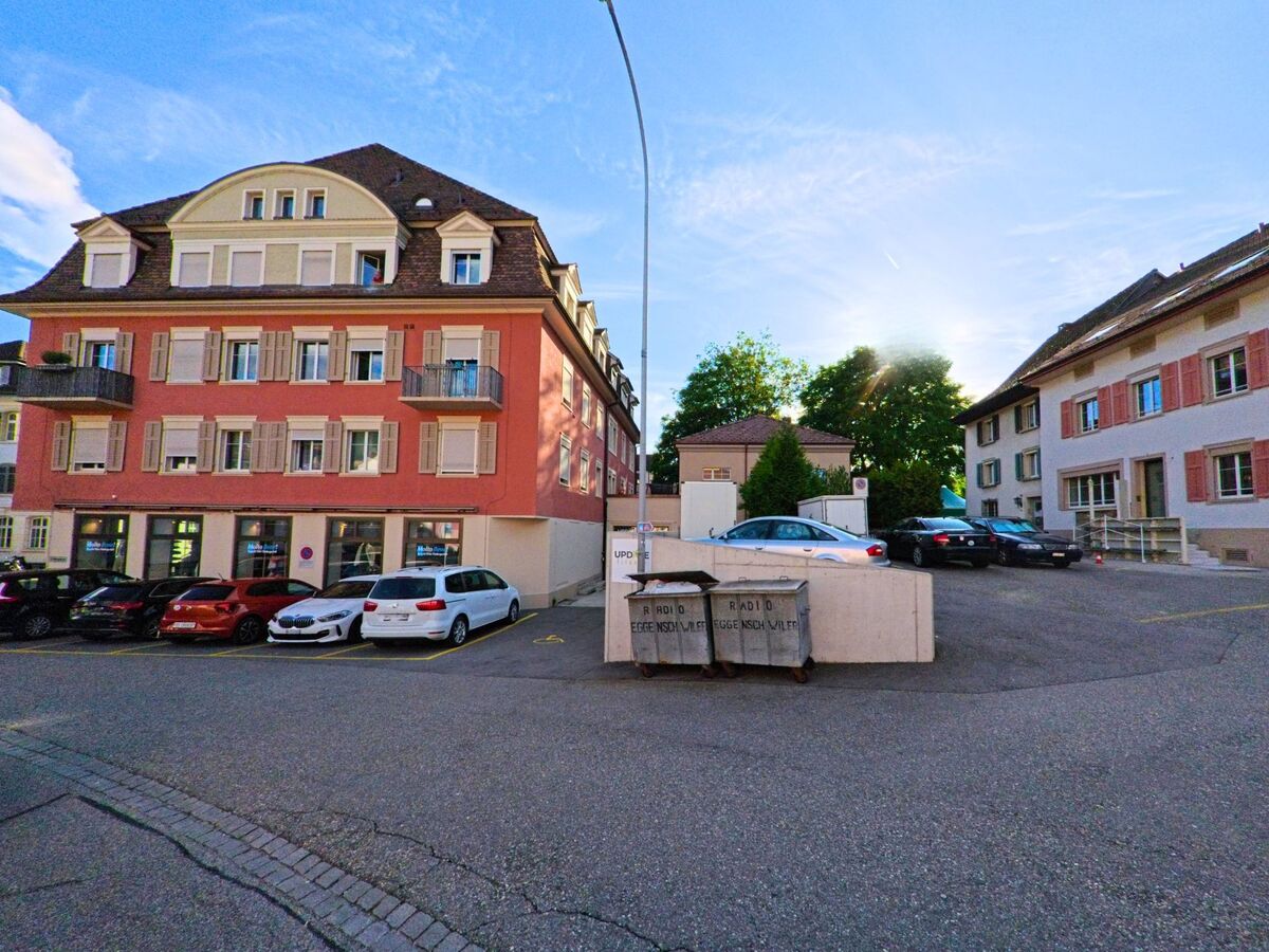 Im Zentrum von Balsthal im Kanton Solothurn, PLZ 4710, stehen mehrstöckige Wohn- und Geschäftshäuser mit bunten Fassaden rund um einen kleinen Parkplatz im Abendlicht.