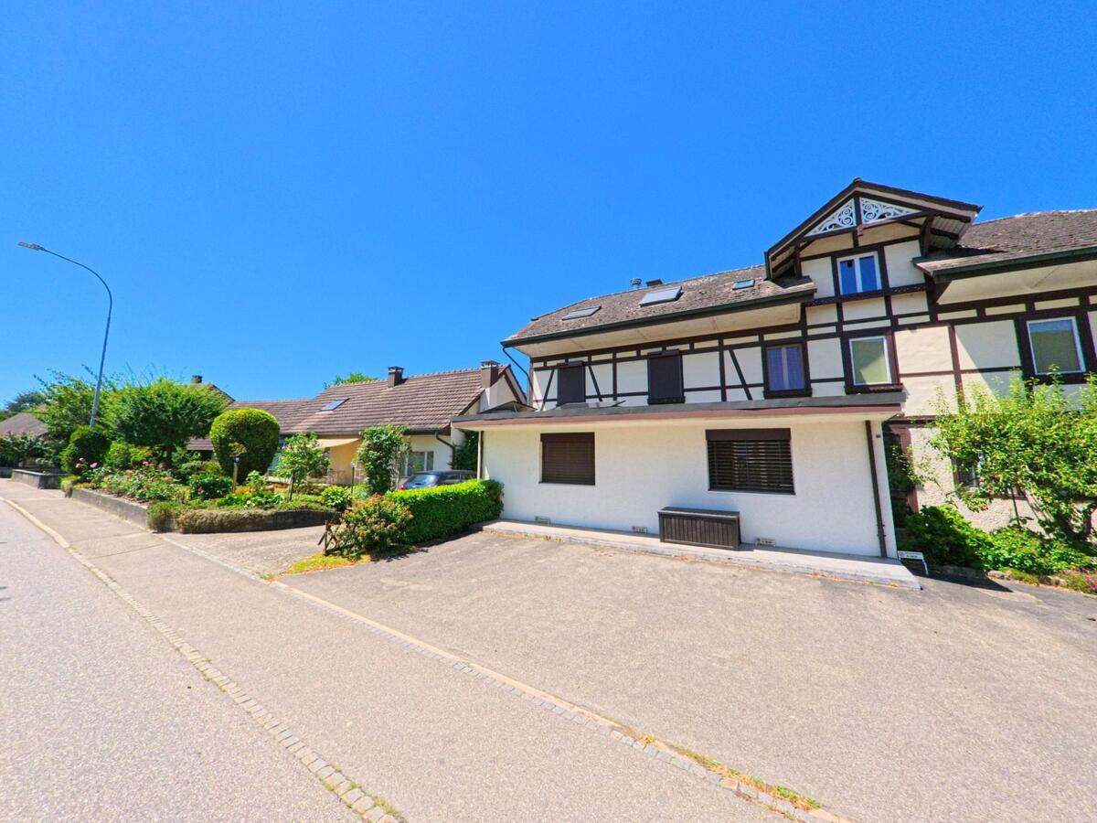 Entlang einer Wohnstrasse in Bannwil (4913, Kanton Bern) stehen gepflegte Einfamilienhaeuser mit Gaerten, darunter auch ein Fachwerkhaus mit markanter Giebelfront.