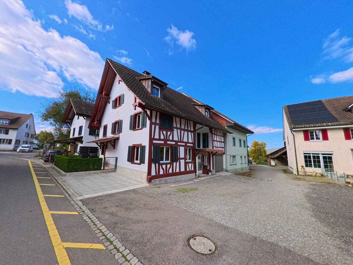 Mehrere historische Wohnhäuser mit sichtbarem Fachwerk stehen an einem offenen Hofbereich in Basadingen-Schlattingen (8254) im Kanton Thurgau unter klarem Himmel.
