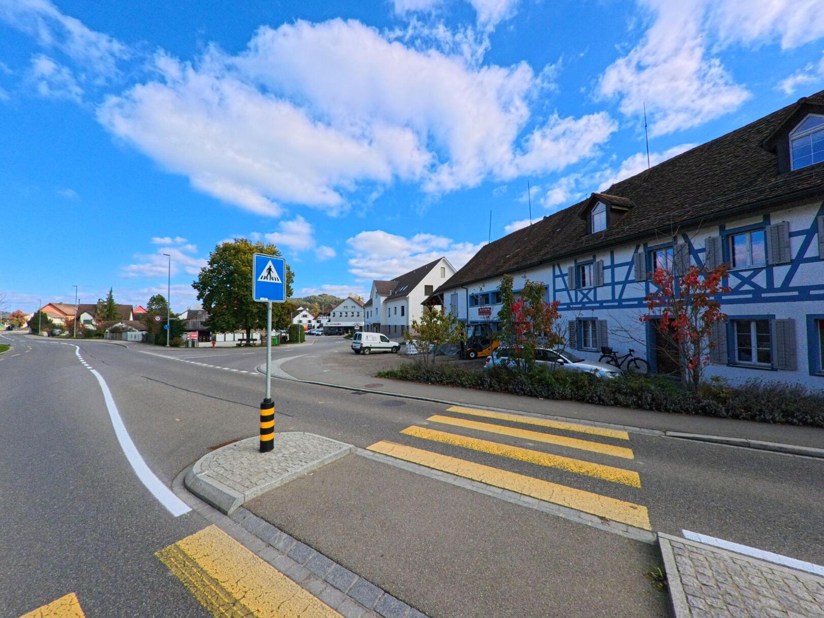 Ein Fussgängerstreifen mit Mittelinsel liegt an einer Dorfstrasse in Basadingen-Schlattingen (8254), Kanton Thurgau, neben traditionellen Wohnhäusern.