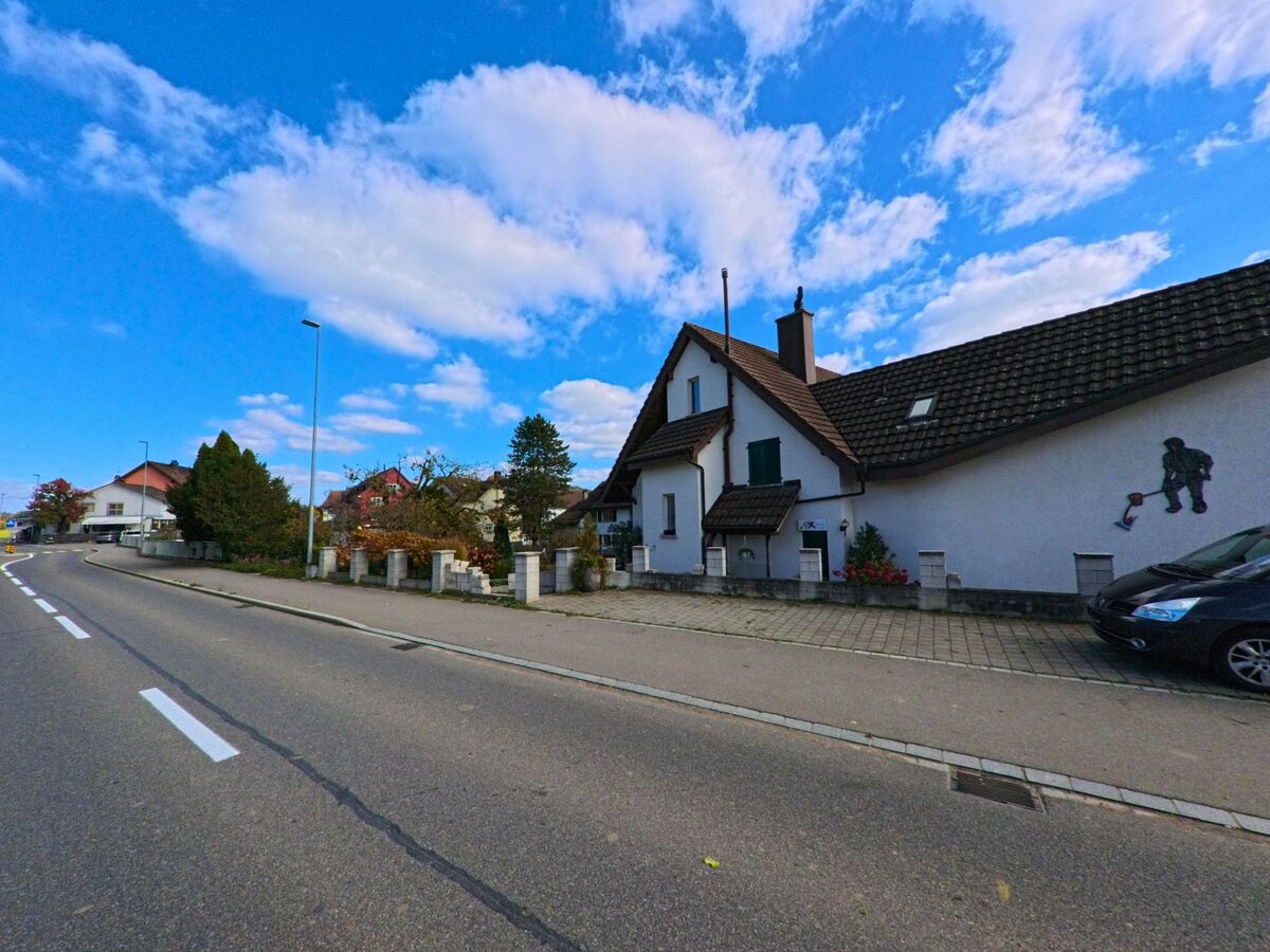 Ein Wohnhaus mit Vorgarten liegt an einer leicht geschwungenen Strasse in Basadingen-Schlattingen (8254) im Kanton Thurgau unter weitem Himmel.