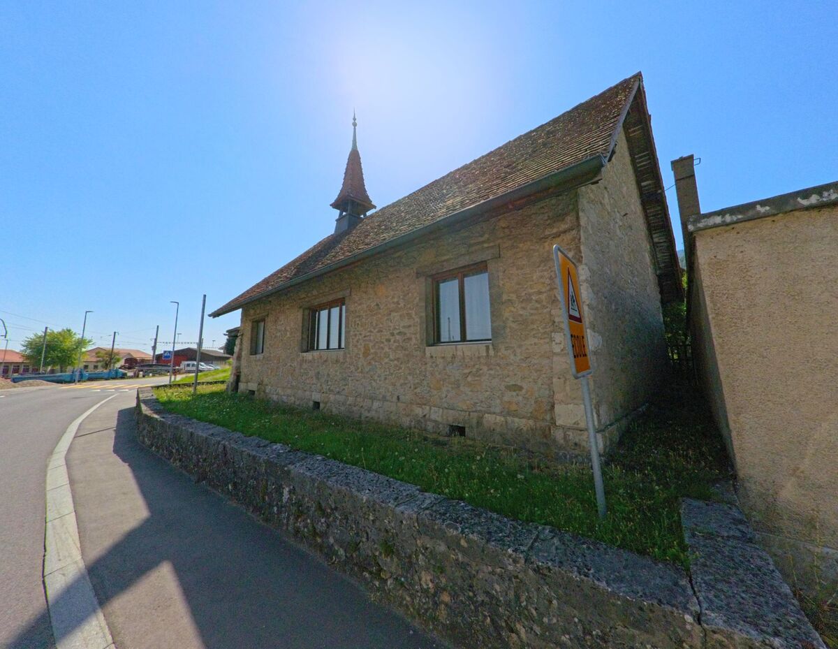 Ein altes Steingebaeude mit kleinem Turm steht in Baulmes (1446, Kanton Waadt) direkt an der Strasse nahe dem Bahnhofsgelaende.