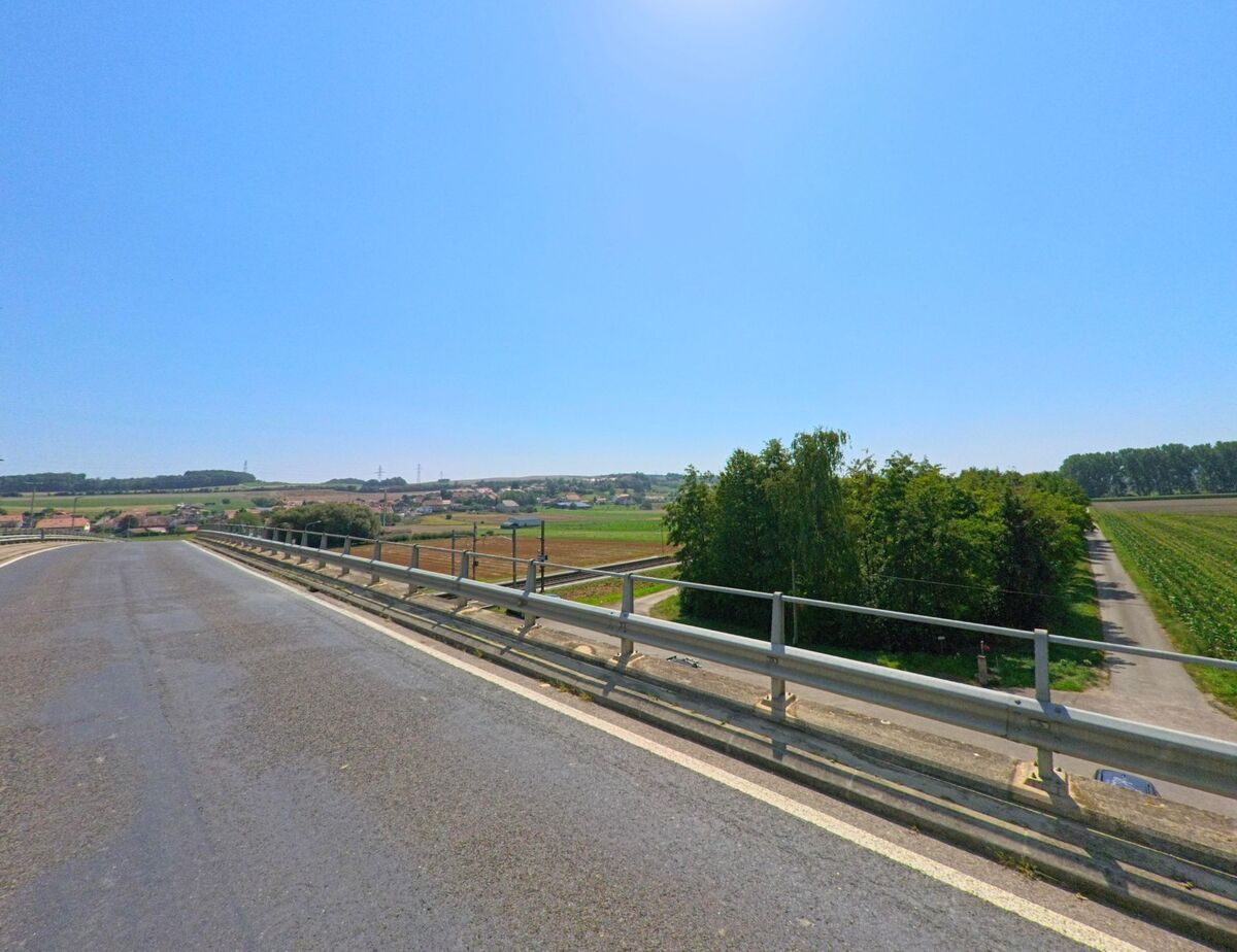 Von einer Bruecke in Bavois (1372, Kanton Waadt) erstreckt sich der Blick ueber Felder, Baeume und das Dorf am Horizont.