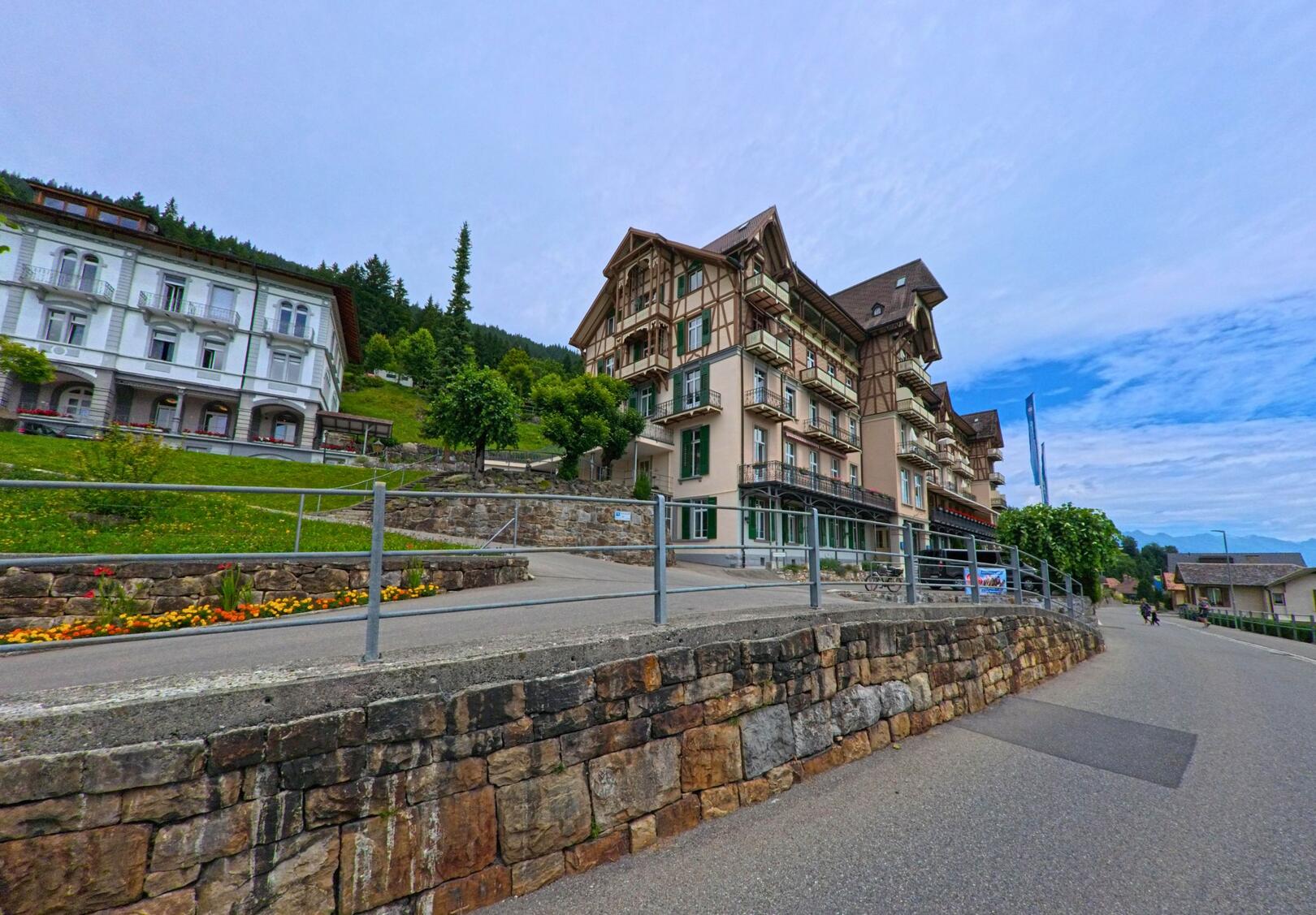 In Beatenberg (3803, Kanton Bern) stehen entlang einer leicht ansteigenden Strasse prächtige Hotelbauten mit Holzverzierungen und Balkonreihen vor bewaldetem Hang.