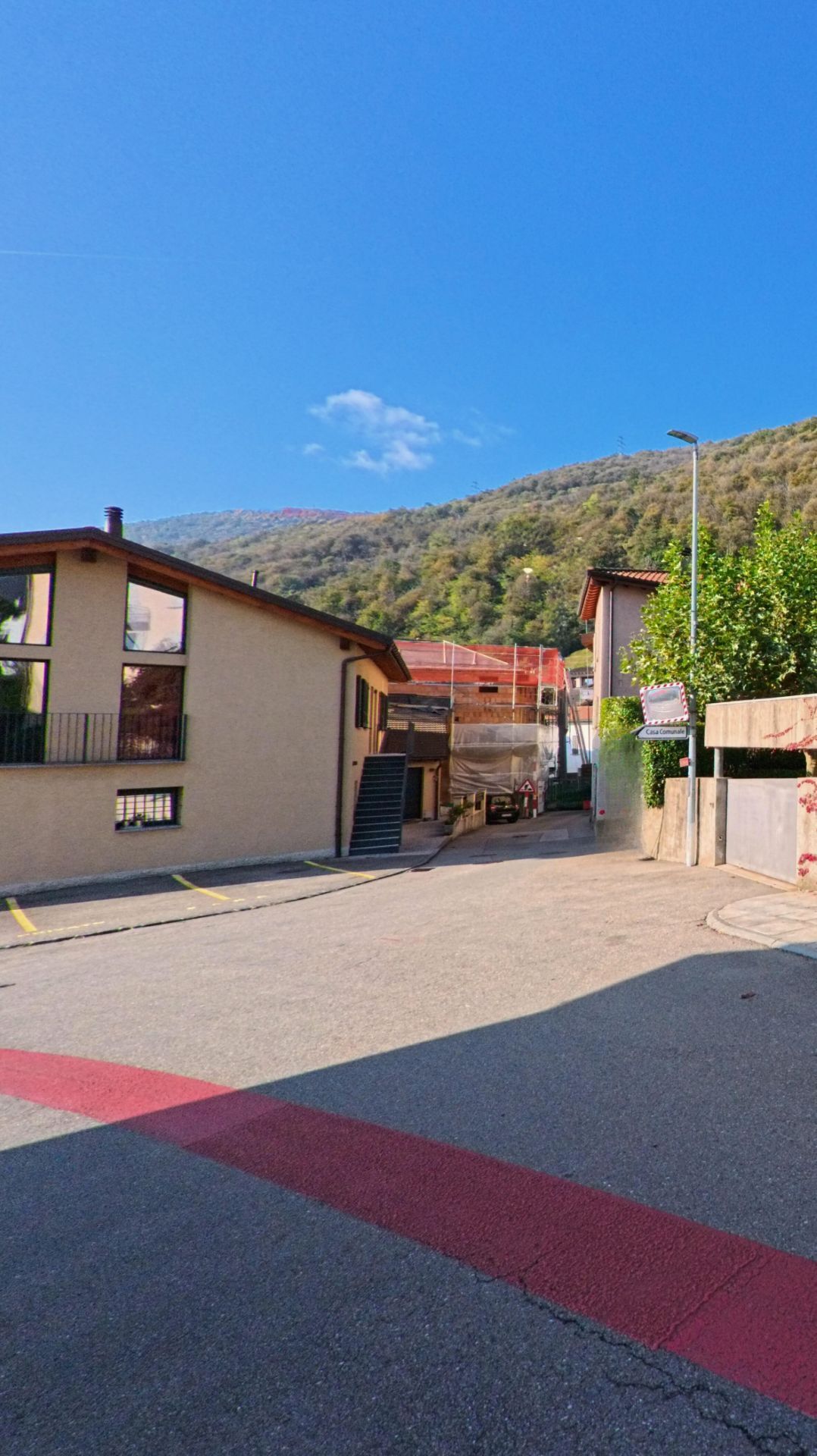Am Ende einer schmalen Quartierstrasse in Bedano (6930, Kanton Tessin) stehen Wohnhaeuser neben einer Zufahrt, waehrend sich dahinter der bewaldete Hang erhebt.