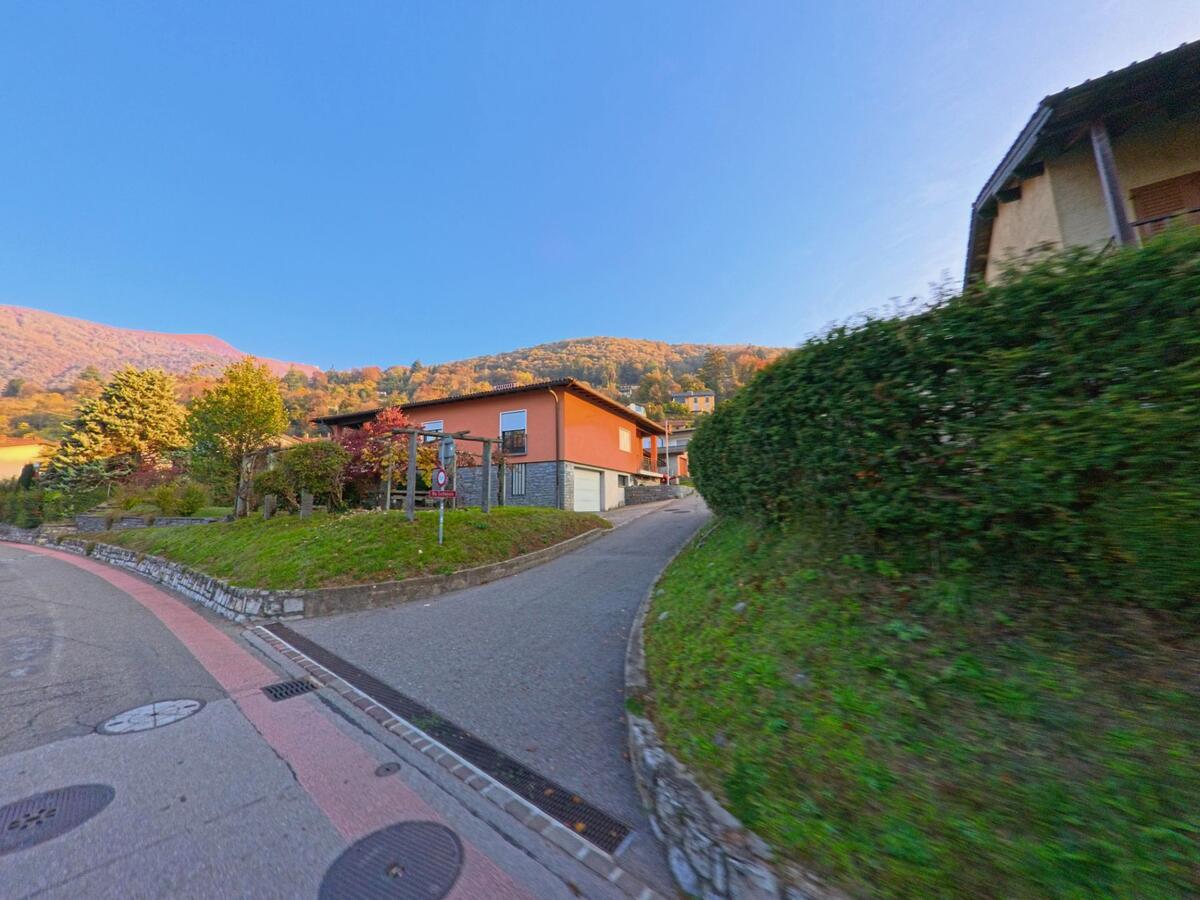 An einer Weggabelung mit ansteigender Zufahrt liegt in Bedigliora (6981, Kanton Tessin) ein Wohnhaus mit Garten vor herbstlich gefaerbten Huegeln.
