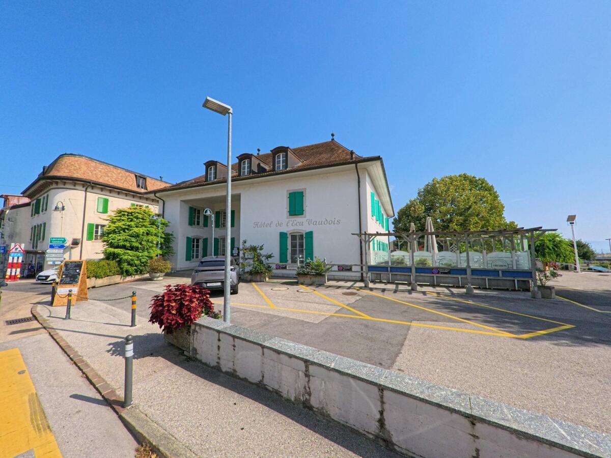 In Begnins (1268, Kanton Waadt) inspiziert ein Kammerjaeger das Hotel de l’Ecu Vaudois mit gruener Fensterlaeden und vorgelagerter Terrasse.