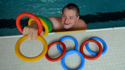 In Volketswil (8604, Kanton Zuerich) spielt ein Schwimmer des Behinderten-Sport Clubs Zuerich lachend im Wasser und legt bunte Schwimmringe am Beckenrand ab.