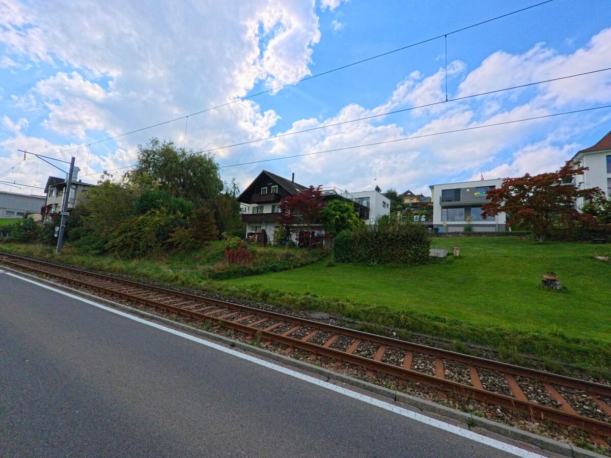 In Beinwil am See (5712, Kanton Aargau) verlaufen die Bahngleise an einem grünen Hang mit modernen und traditionellen Wohnhäusern entlang.