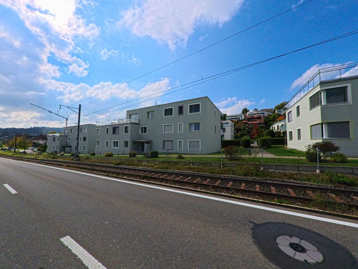 Mehrere moderne Wohnhäuser mit flachen Dächern liegen entlang der Bahnlinie in Beinwil am See (5712, Kanton Aargau) unterhalb eines begrünten Hanges.