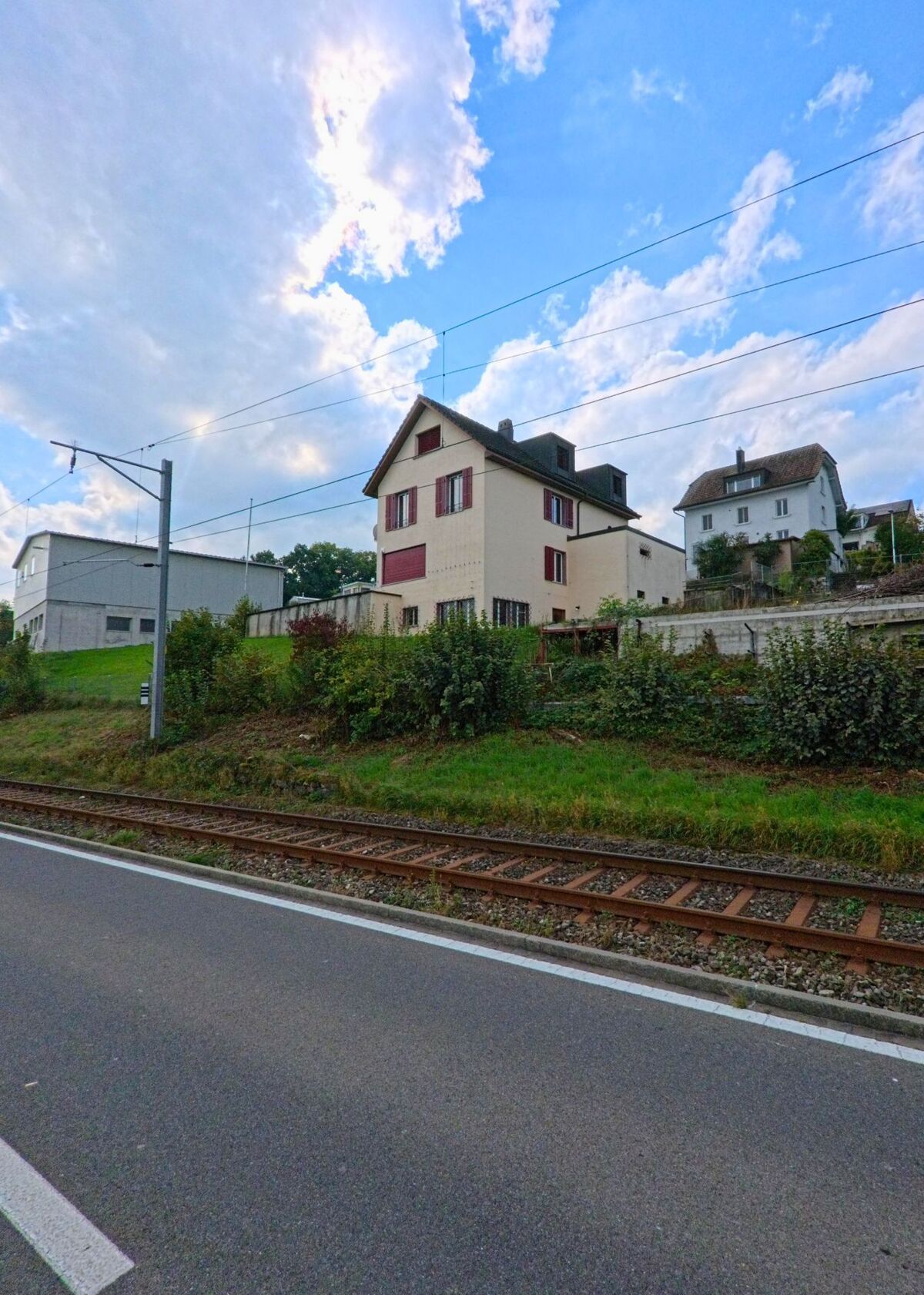 Ein mehrstöckiges Wohnhaus mit roten Fensterläden steht oberhalb der Bahnlinie in Beinwil am See (5712, Kanton Aargau), flankiert von weiteren Häusern am Hang.