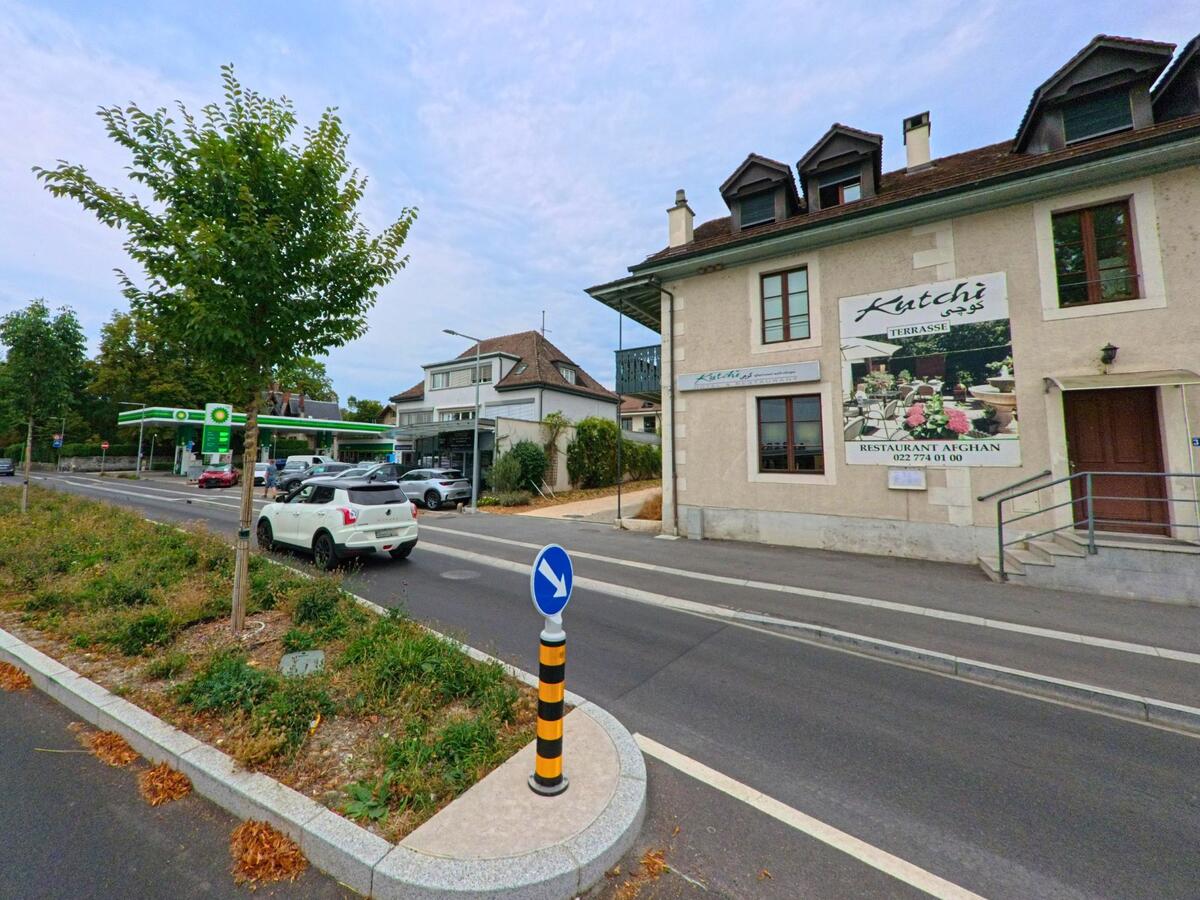 An der Hauptstrasse in Bellevue (1293, Kanton Genf) liegt ein afghanisches Restaurant neben einer Tankstelle, davor fuehren Fahrspuren mit Verkehrsinsel vorbei.