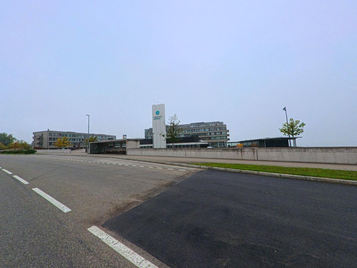Die Rehaklinik Bellikon (5454, Kanton Aargau) erhebt sich mit modernen Gebäuden und klarer Architektur über der Strasse unter grauem Himmel.