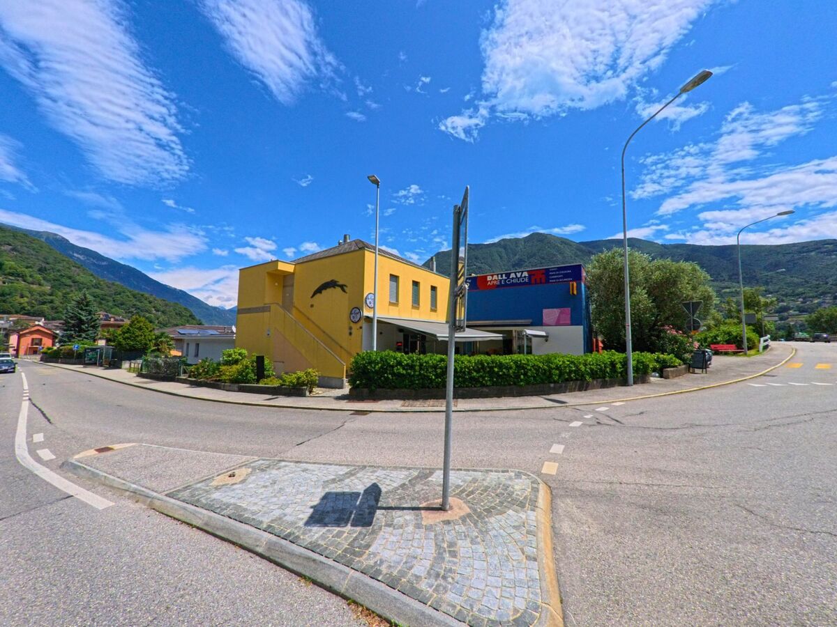 An einer Strassenkreuzung in Bellinzona (6503, Kanton Tessin) steht ein gelbes Gebaeude mit einer Bar und Blick auf die umliegenden Berge.