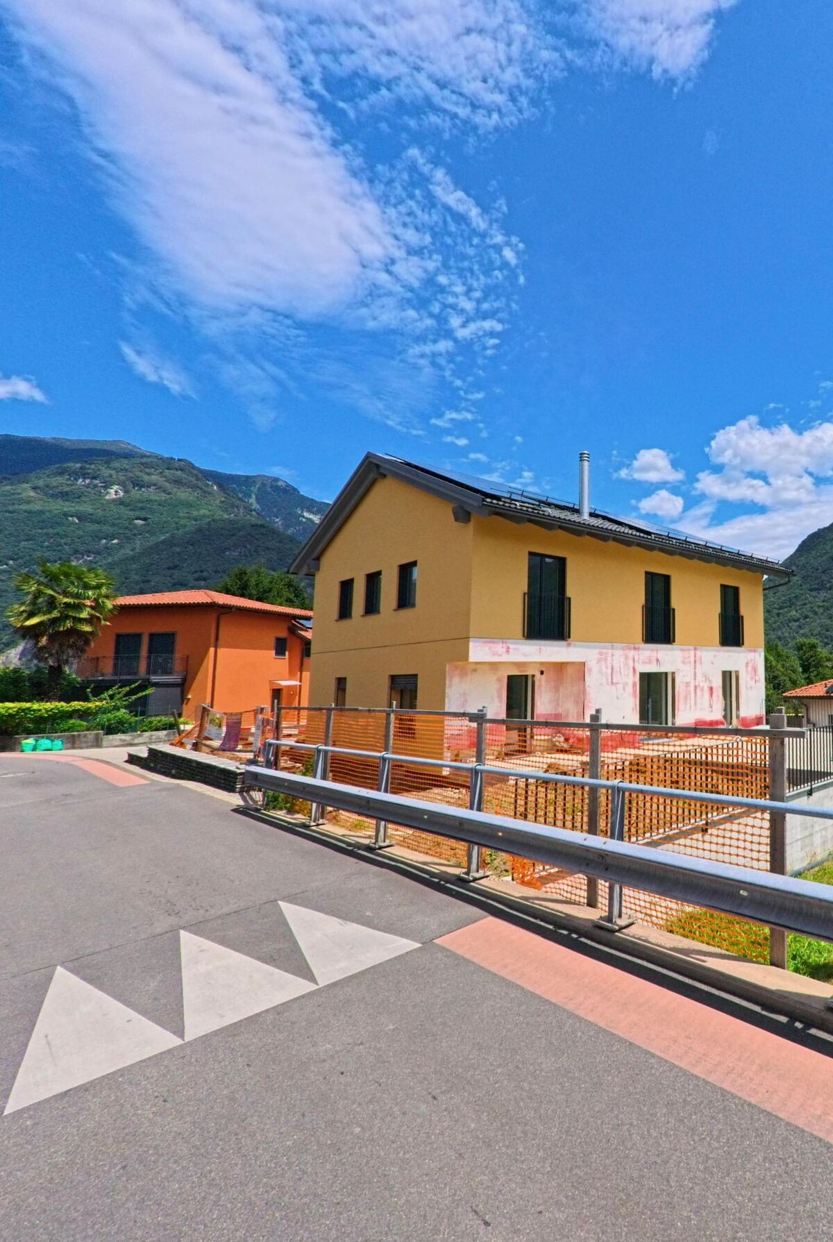 Ein hellgelbes Wohnhaus in Bellinzona (6503, Kanton Tessin) steht am Strassenrand mit Blick auf die bewaldeten Berghaenge und wird teilweise renoviert.