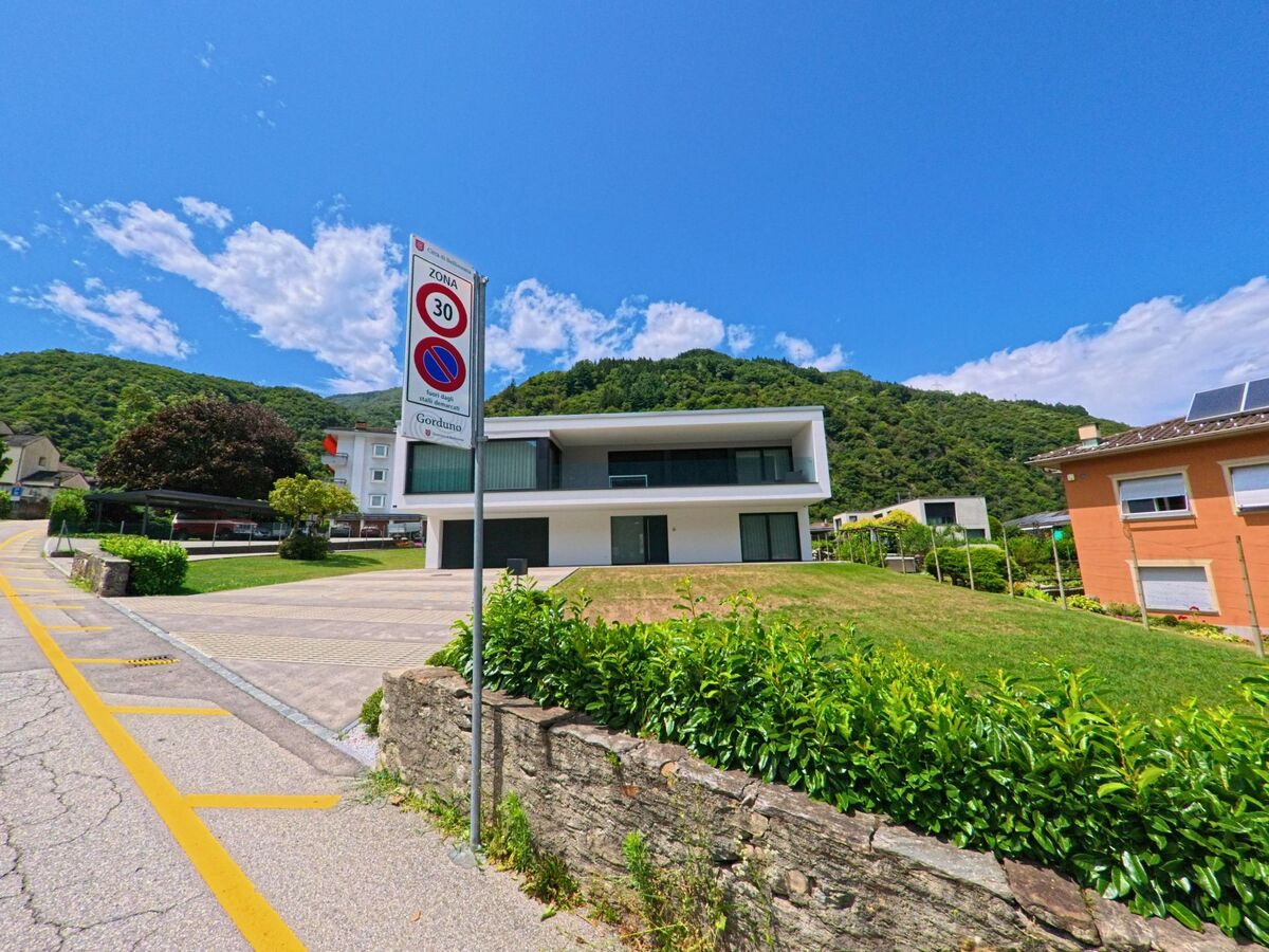 In Bellinzona (6518, Kanton Tessin) steht ein modernes Wohnhaus mit grossen Fenstern an einer ruhigen Strasse im Ortsteil Gorduno, umgeben von gruener Hügellandschaft.