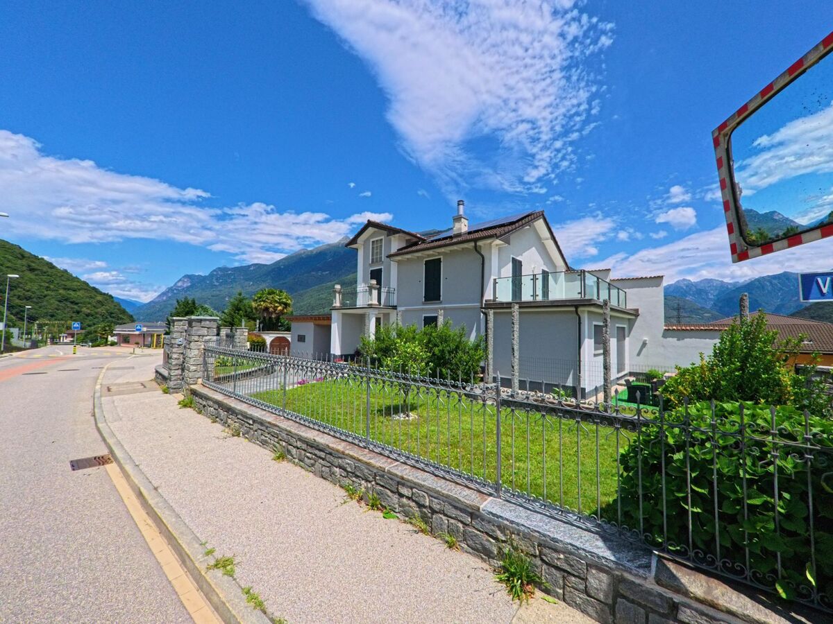 Ein weisses Wohnhaus mit Balkon und Garten steht in Bellinzona (6518, Kanton Tessin) an einer ruhigen Strasse mit Blick auf die umliegenden Berge des Tales.