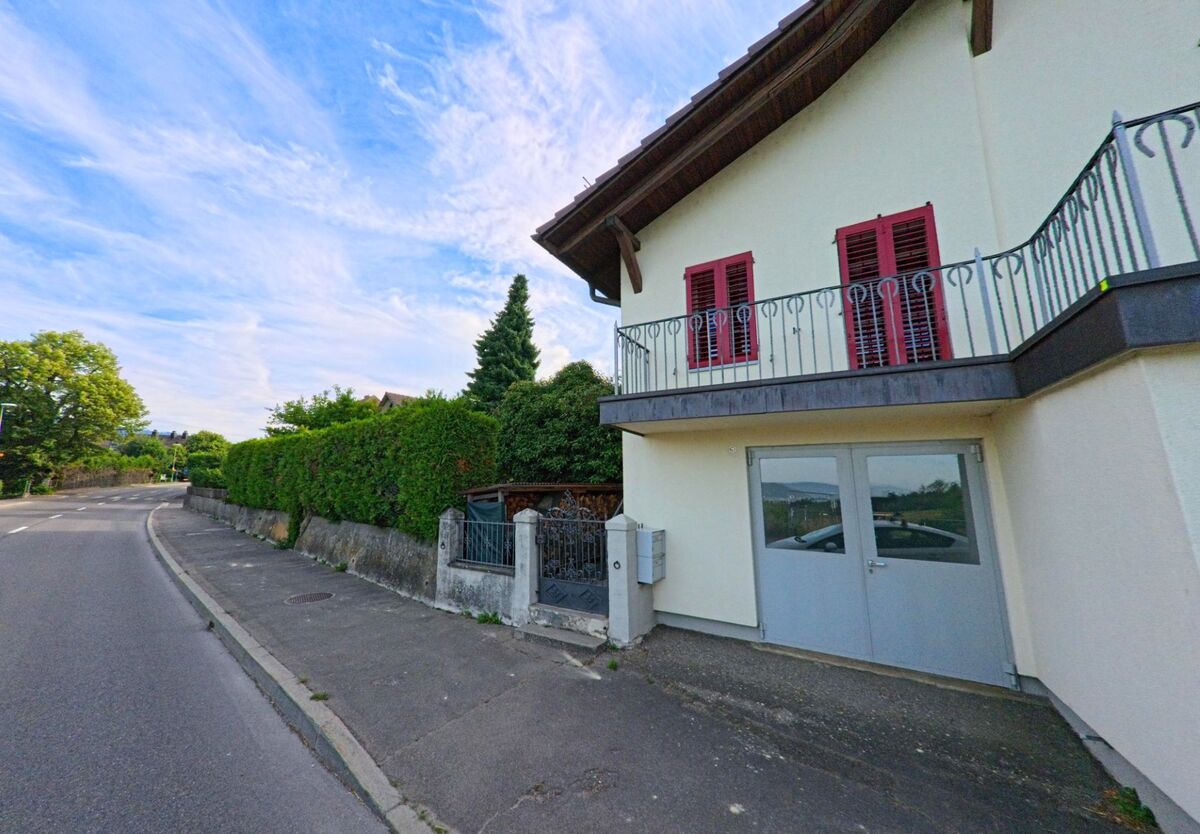 In Bellmund (2564, Kanton Bern) steht ein modernes Wohnhaus mit einem gepflegten Garten, das von einer Hecke umgeben ist. Die Straße verläuft parallel zu der Immobilie.