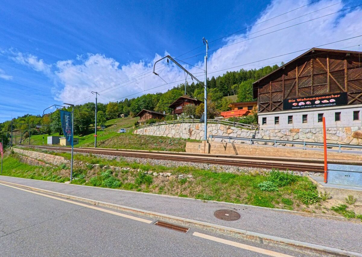 Am Rand von Bellwald (3997, Kanton Wallis) steht ein Holzgebäude neben einer Scheune mit grossen Solarpanelen vor den Bergen.