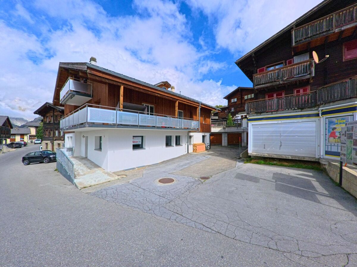 In Bellwald (3997, Kanton Wallis) stehen moderne und traditionelle Holzhäuser nebeneinander an einer gepflasterten Strasse mit Parkplätzen.