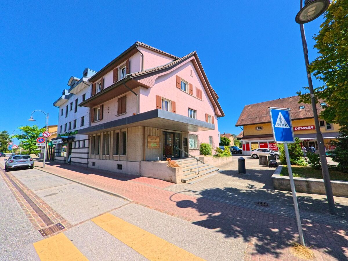 In Belmont-Broye (1564, Kanton Freiburg) befinden sich an einer Strasse mit Zebrastreifen mehrere Geschaefte, darunter ein Lebensmittelmarkt und eine Apotheke.