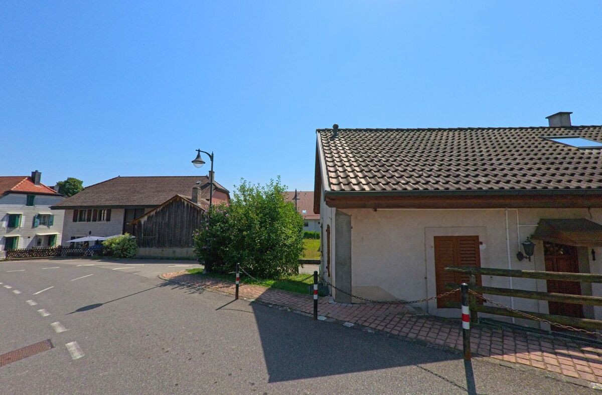 In Belmont-sur-Yverdon (1432, Kanton Waadt) stehen Wohnhaeuser mit traditionellen Daechern an einer Strassenkurve im Dorfzentrum.