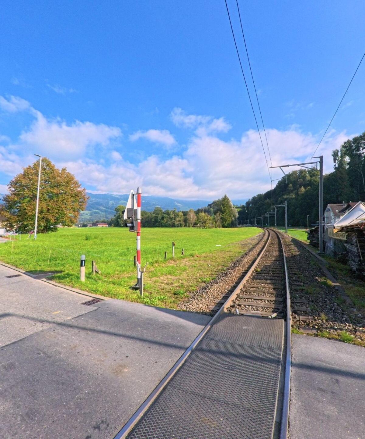 Ein Bahnuebergang mit Gleisen fuehrt durch offene Wiesen und verbindet die Umgebung in Benken (8717, Kanton St. Gallen) bei klarer Sicht.