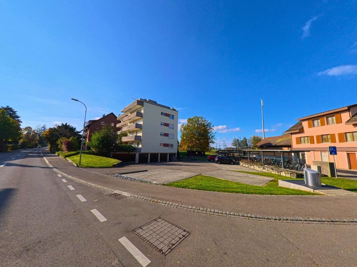 Ein Mehrfamilienhaus mit Balkonen und angrenzenden Parkflächen prägt das Wohnumfeld entlang einer Strasse in Berg (8572, Kanton Thurgau) bei klarem Herbstwetter.