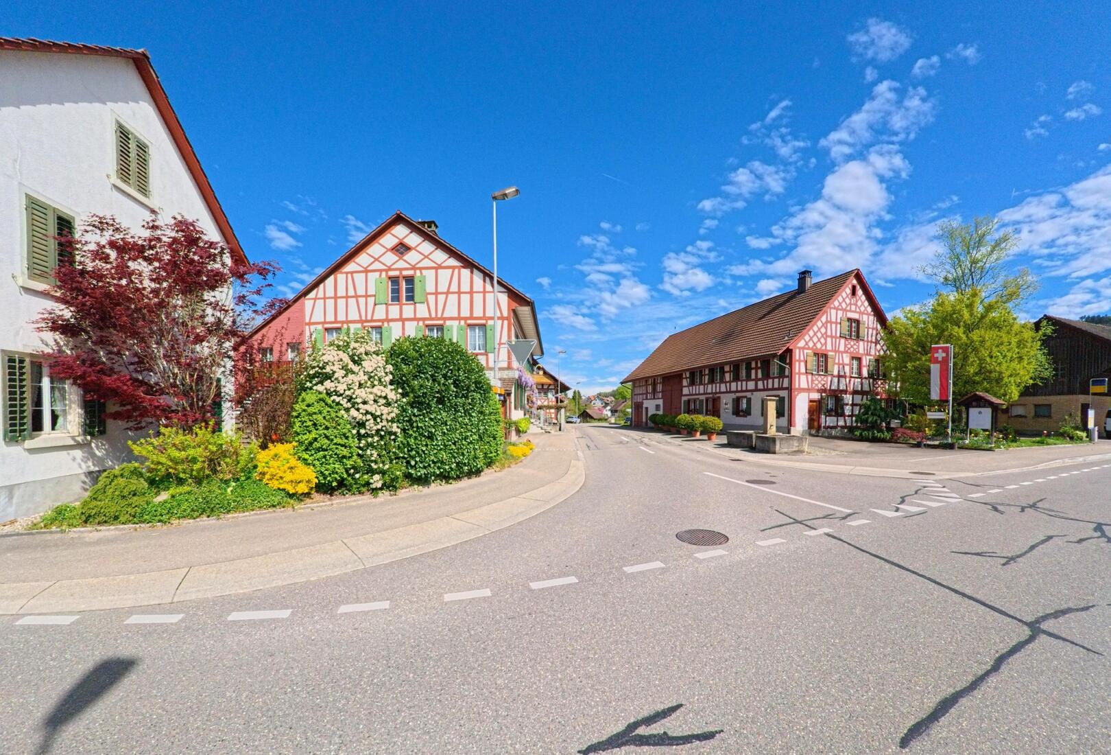 Zwei markante Fachwerkhäuser prägen das Ortsbild von Berg am Irchel (8415, Kanton Zürich) an einer zentralen Kreuzung mit gepflegter Bepflanzung und klarer Sichtachse durchs Dorf.