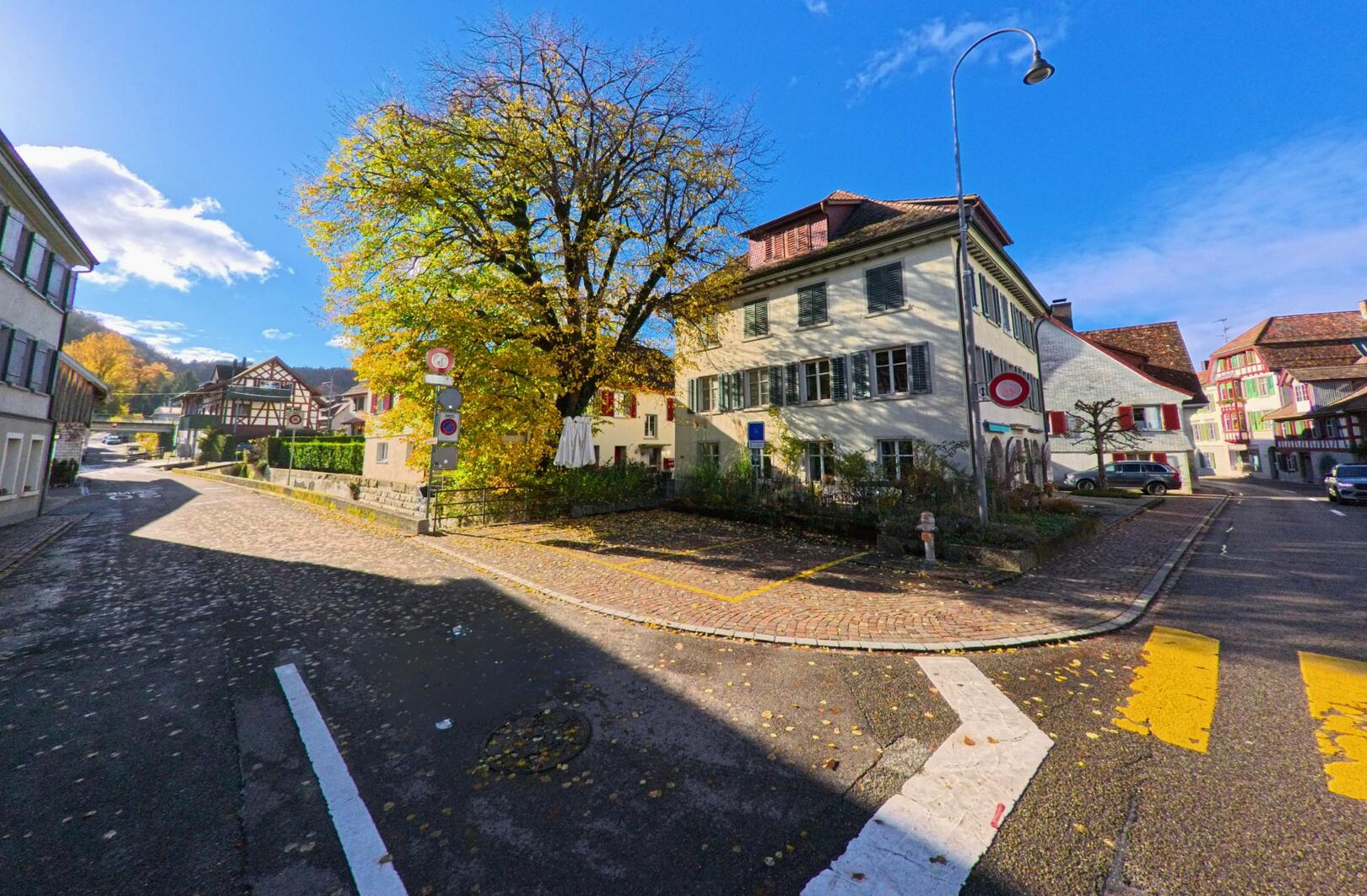 An einer ruhigen Strassenkreuzung mit historischen Wohnhäusern zeigt sich das Dorfzentrum von Berlingen (8267, Kanton Thurgau) unter blauem Himmel und herbstlichem Baumbestand.