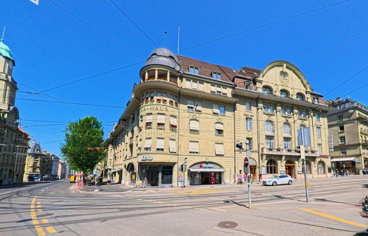 In Bern (3011, Kanton Bern) steht ein markantes historisches Gebäude mit der Aufschrift „KA-HAUS“ an einer vielbefahrenen Kreuzung mit Tramlinien und Geschäften im Erdgeschoss.