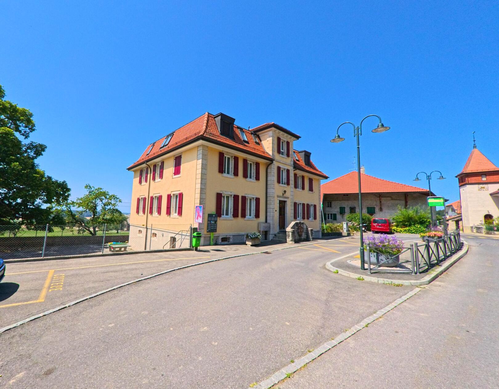 Vor dem Gemeindehaus in Berolle (1149, Kanton Waadt) verläuft eine Strasse mit Randbepflanzung und Laternen.