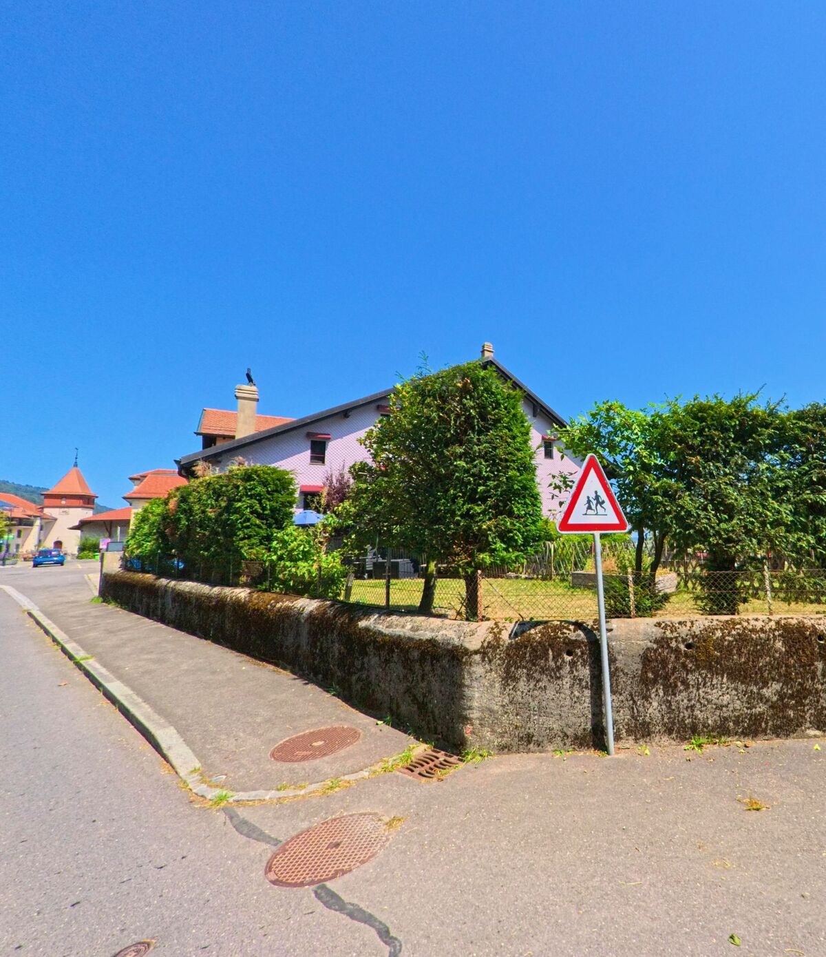 Ein Schulweg-Schild steht am Strassenrand vor einem Wohnhaus mit Garten in Berolle (1149, Kanton Waadt).