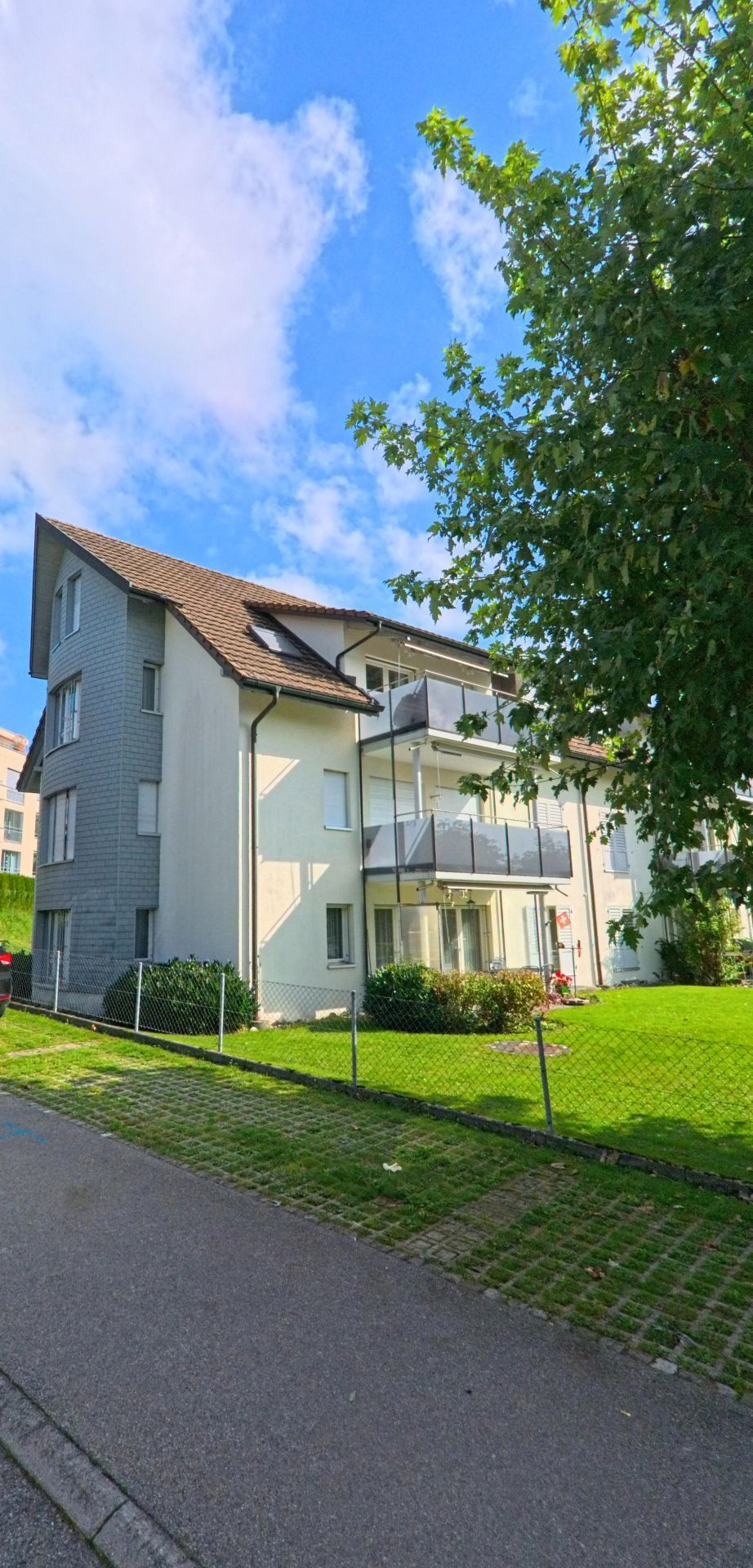 In Beromuenster (6215, Kanton Luzern) steht ein mehrstöckiges Wohnhaus mit Balkonen neben einer gepflegten Gruenflaeche und einem schmalen Gehweg.